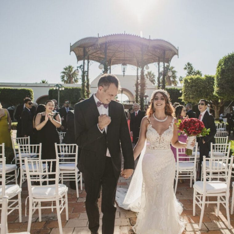 Pareja de recién casados saliendo de la ceremonia al aire libre, rodeados de invitados.