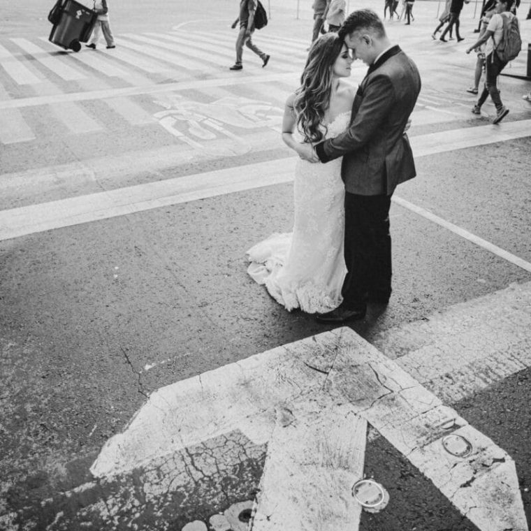 Novios besándose en un cruce urbano, fotografía de boda en la ciudad en blanco y negro.